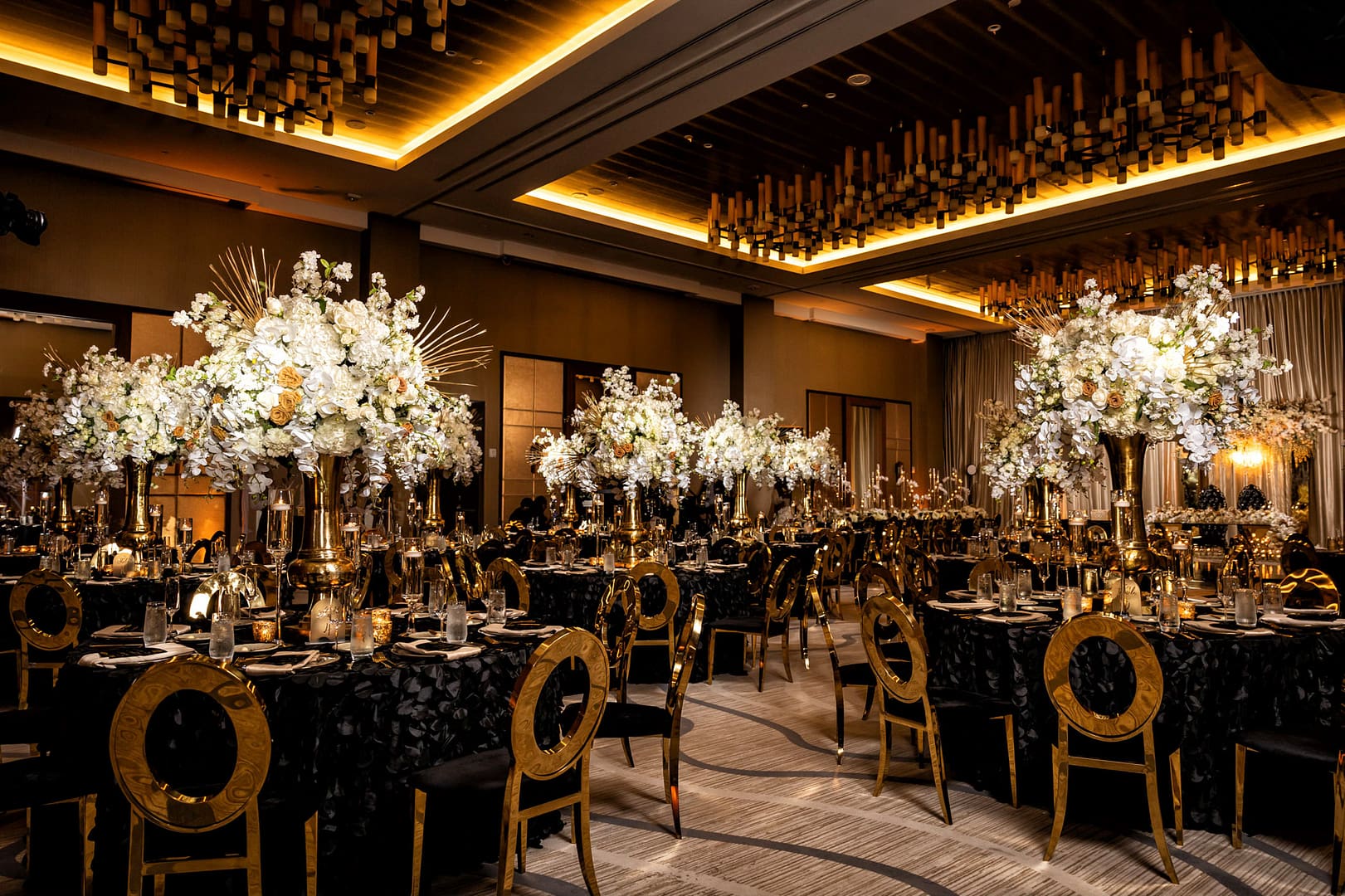 Extravagant Black and Gold Wedding Ceremony with Gold Chairs, Black Linens, and White Floral Centerpieces 