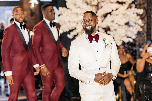 Groom Walking Down the Aisle in Cream Tuxedo with Burgundy Bow Tie Followed by Groomsmen in Burgundy Wedding Portrait | Photographer Stanlo Photography