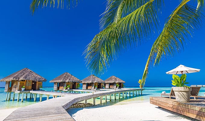 Luxury hotel with water villas and palm tree leaves over white sand, close to blue sea, seascape in Maldives.