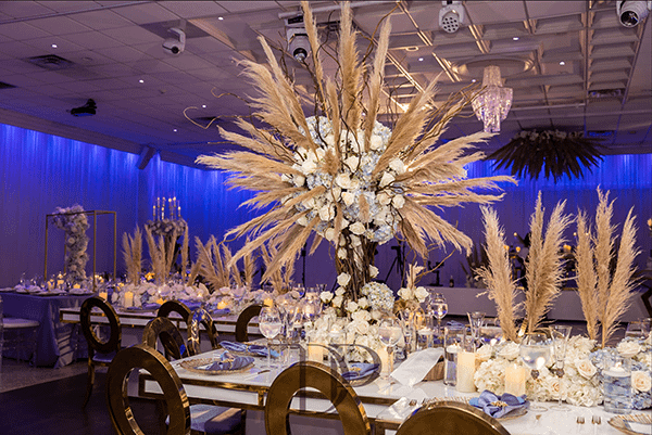 Ballroom Wedding Reception with Large Pampas Centerpieces, Gold Chairs, and Blue Mood Lighting Ballroom Wedding Reception with Large Pampas Centerpieces, Gold Chairs, and Blue Mood Lighting